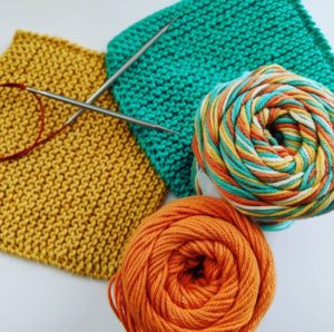 Photo: One yellow and one green washcloth, along with a set of circular knitting needles, and skeins of orange and multicolor cotton yarn.